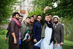 grupo de hombres paquistaníes vestidos con ropa tradicional salwar kameez o kurta haciendo selfie en el teléfono móvil. foto