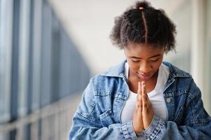 African woman in jeans jacket pray indoor. photo