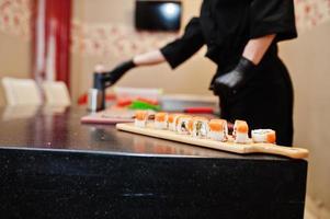 Cierra las manos de un chef profesional con guantes negros haciendo sushi y rollos en la cocina de un restaurante de comida tradicional japonesa. foto