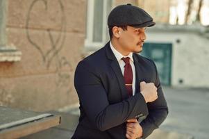 Portrait of retro 1920s english arabian business man wearing dark suit, tie and flat cap. photo