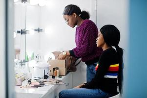 African American woman applying make-up by make-up artist at beauty saloon. photo