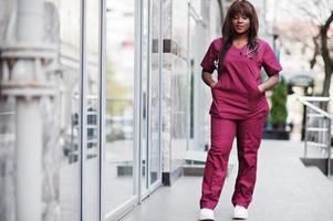 doctora afroamericana en uniforme de laboratorio rojo con máscara facial protectora. concepto de medicina, profesión y atención médica. foto