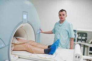 Male doctor turns on magnetic resonance imaging machine with patient inside. photo
