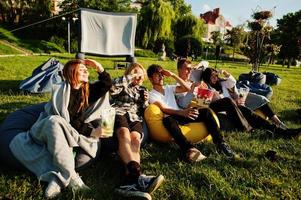 Young multi ethnic group of people watching movie at poof in open air cinema. photo