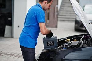Car repair and maintenance theme. Mechanic in uniform working in auto service, changing car battery. photo