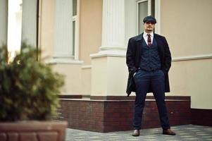 Portrait of retro 1920s english arabian business man wearing dark coat, suit, tie and flat cap. photo