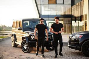 Two asian brothers man wear on all black posed near suv cars. photo