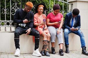 Four african friends having fun outdoors. Two black girls with guys with mobile phones. photo