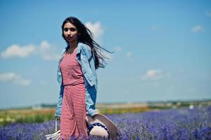 Beautiful indian girl in summer dress and jeans jacket in purple lavender field with basket in hand and hat. photo
