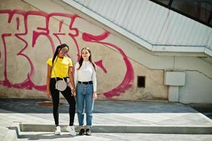 niña caucásica blanca y afroamericano negro juntos contra la pared de graffiti. unidad mundial, amor racial, comprensión en la tolerancia y cooperación en la diversidad de razas. foto