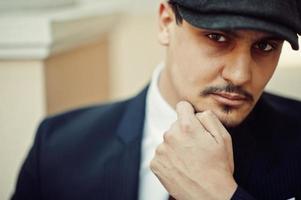 Portrait of retro 1920s english arabian business man wearing dark suit, tie and flat cap. photo