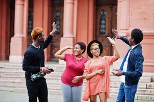 Four african friends having fun outdoors. Two black girls give high five to guys. photo