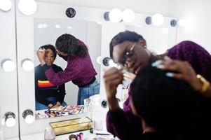 African American woman applying make-up by make-up artist at beauty saloon. photo