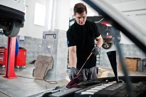 Car repair and maintenance theme. Mechanic in uniform working in auto service, checking engine. photo