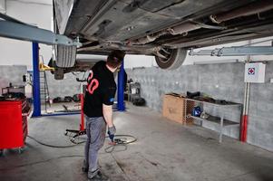 Car repair and maintenance theme. Mechanic in uniform working in auto service. photo
