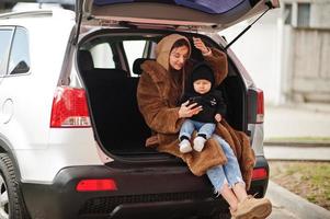 Young mother and child sitting in the trunk of a car and looking at mobile phone. Safety driving concept. photo