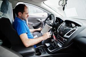 Car repair and maintenance theme. Electric mechanic in uniform working in auto service, making car diagnostics using obd device with laptop. photo