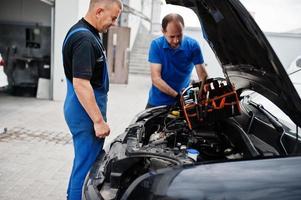 Car repair and maintenance theme. Two mechanics in uniform working in auto service, checking engine. photo