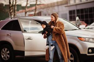 la joven madre y el niño se paran cerca de su auto todoterreno. concepto de conducción segura. foto