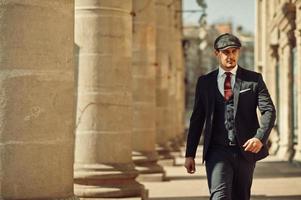 Portrait of retro 1920s english arabian business man wearing dark suit, tie and flat cap near old columns. photo