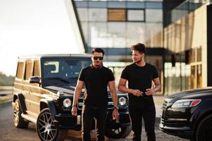 Two asian brothers man wear on all black posed near suv cars. photo