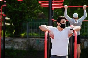 Portrait sports arabian man in black medical face mask doing workout exercises in outdoor gym place during coronavirus quarantine. photo