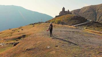 Luftfliege über weibliche Touristen, die einen Panoramablick auf die Dreifaltigkeitskirche von Gergeti auf dem Hügel genießen. georgien urlaub und sehenswürdigkeiten im kaukasus. video
