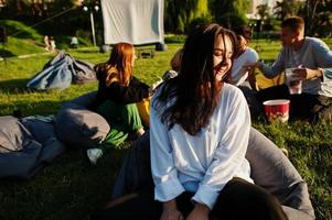 Young multi ethnic group of people watching movie at poof in open air cinema. Close up portrait of funny girl. photo