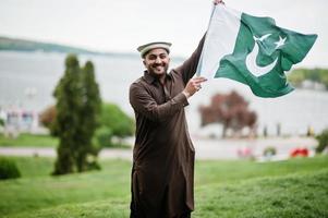 pakistaní pathan el hombre usa ropa tradicional y sostiene la bandera de pakistán. foto