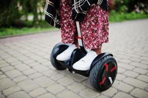 Close up legs of african american woman using segway or hoverboard. Black girl on dual wheel self balancing electrical scooter. photo