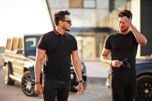 Two asian brothers man wear on all black posed near suv cars. photo