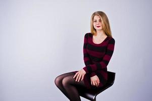 retrato de una mujer joven con un vestido morado a rayas sentado en la silla del estudio. foto