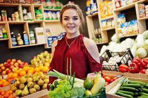 chica de rojo con diferentes verduras en la tienda de frutas. foto