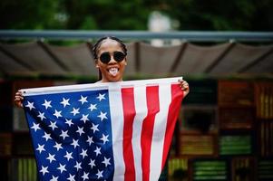 elegante mujer afroamericana con gafas de sol posadas al aire libre con la bandera de estados unidos. foto