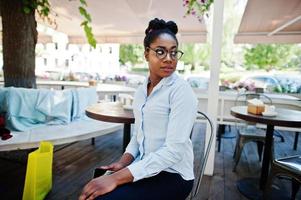 African american girl wear in glasses with mobile phone sitting at outdoor caffe. photo