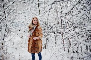 Portraiy of blonde girl in glasses, red fur coat and scarf at winter day. photo