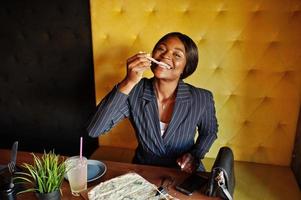 African american businesswoman eating cheese pizza in cafe. Black girl having rest. photo