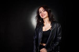 Studio portrait of sexy brunette girl in black leather jacket against black background. photo