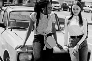 White caucasian girl and black African American together against old retro car. World unity, racial love, understanding in tolerance and races diversity cooperation. photo