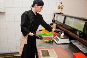 chef profesional vestido de negro haciendo sushi y rollos en la cocina de un restaurante de comida tradicional japonesa. foto