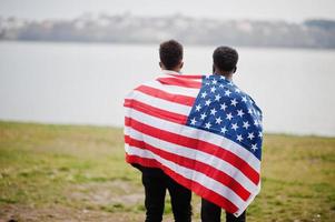 Two african teenagers friends with american flag at park wearing medical masks protect from infections and diseases coronavirus virus quarantine. photo