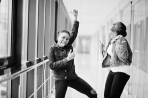 Two african woman friends in jeans jacket show rock fingers  indoor together. photo