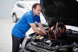 Car repair and maintenance theme. Mechanic in uniform working in auto service, checking engine. photo