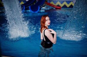 Sexy red haired girl in black swimsuit having rest in swimming pool of aqua park. photo