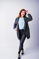 retrato de una fantástica chica pelirroja con camisa azul, abrigo gris posando con gafas de sol en el estudio. foto