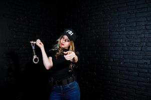 FBI female agent in cap and with gun at studio against dark brick wall. photo