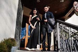 Lovely indian couple in love, wear at saree and elegant suit, posed outdoor terrace on summer sunny day, walking downstairs and hold hands together. photo