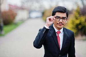 Indian young man at glasses, wear on black suit with red tie posed outdoor. photo