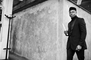 Strong powerful african american man in black suit and turtleneck and cap, with elephant tusk. photo