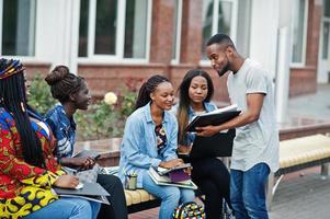 Group of five african college students spending time together on campus at university yard. Black afro friends studying at bench with school items, laptops notebooks. photo